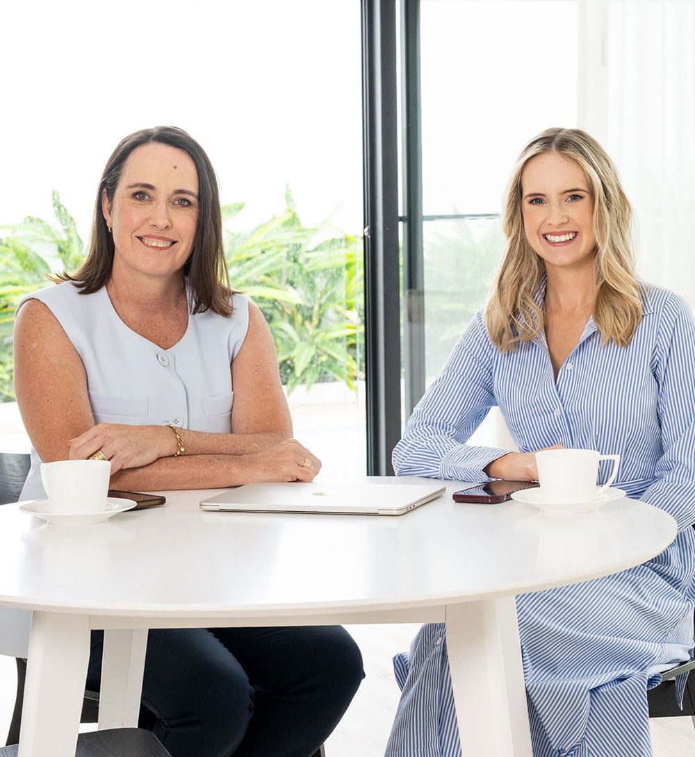 Leanne and Amelia smiling sitting at table in well lit room with a coffee